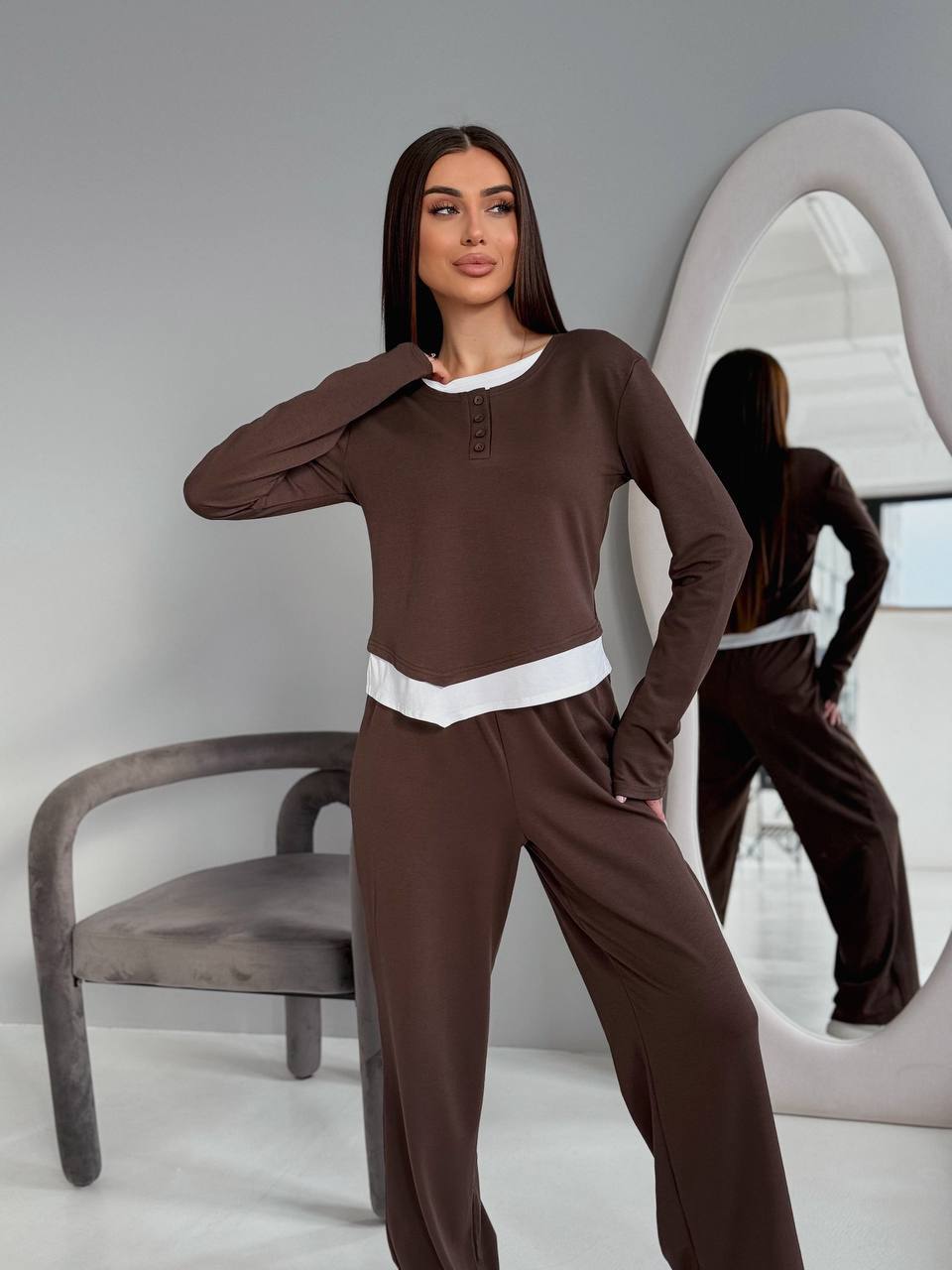 Woman wearing a brown outfit with a white belt in a minimalistic room.