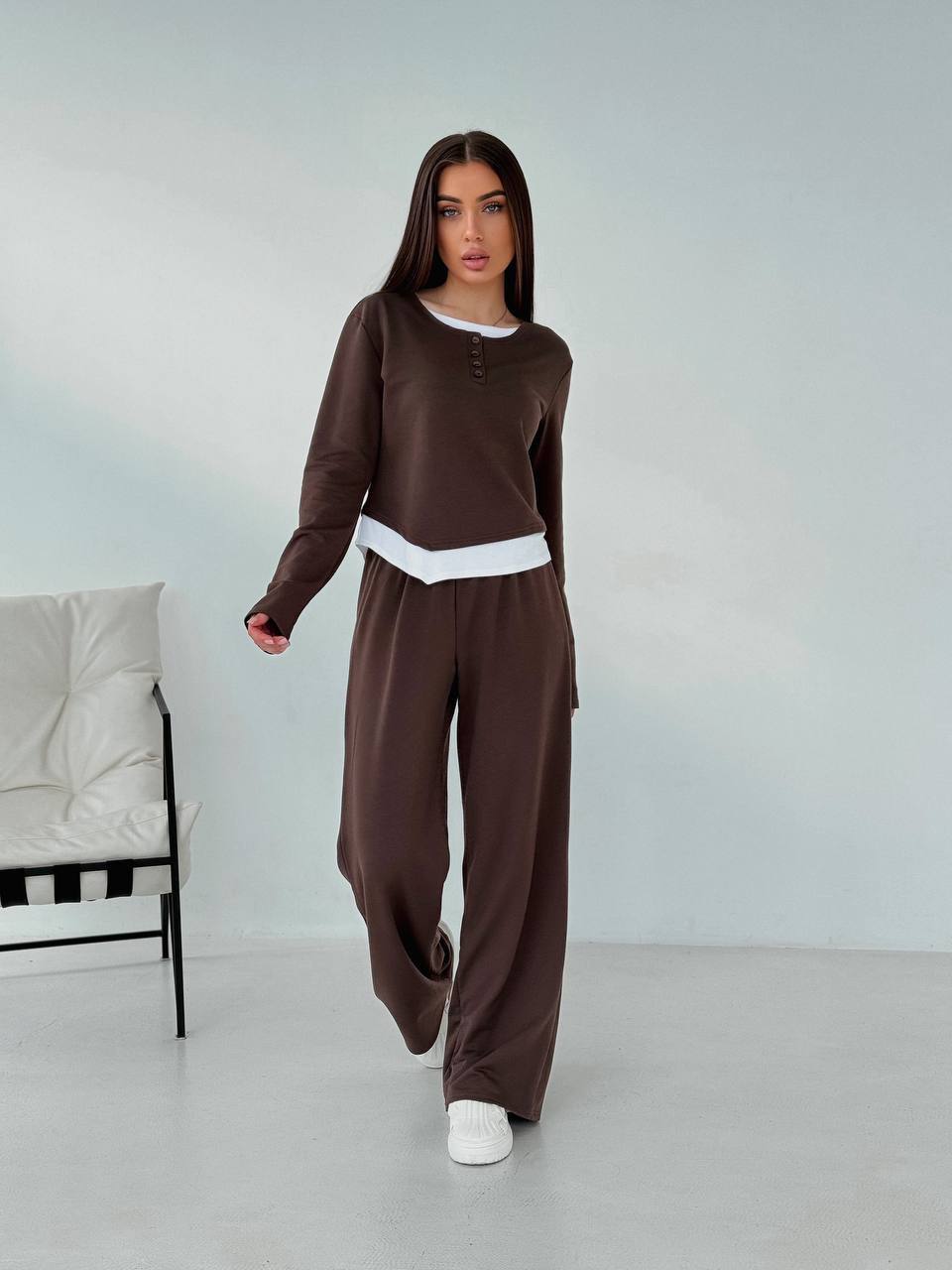 Woman wearing a brown outfit with a white chair in the background