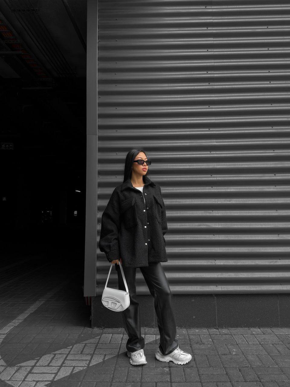 Person wearing a black jacket and pants holding a white bag against a dark background