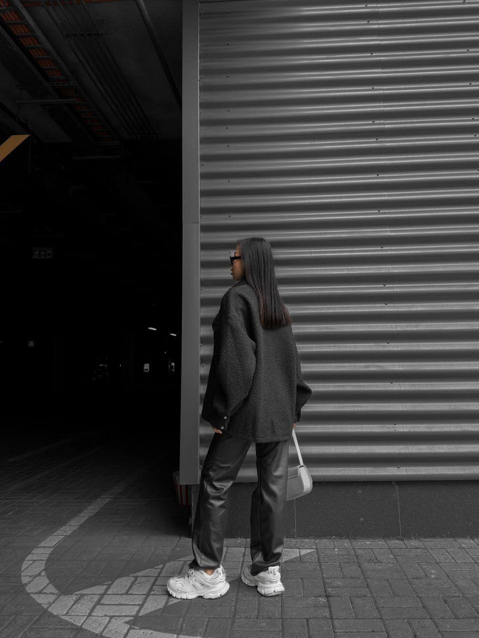 Person wearing a dark hoodie and pants standing in front of a closed shutter door.
