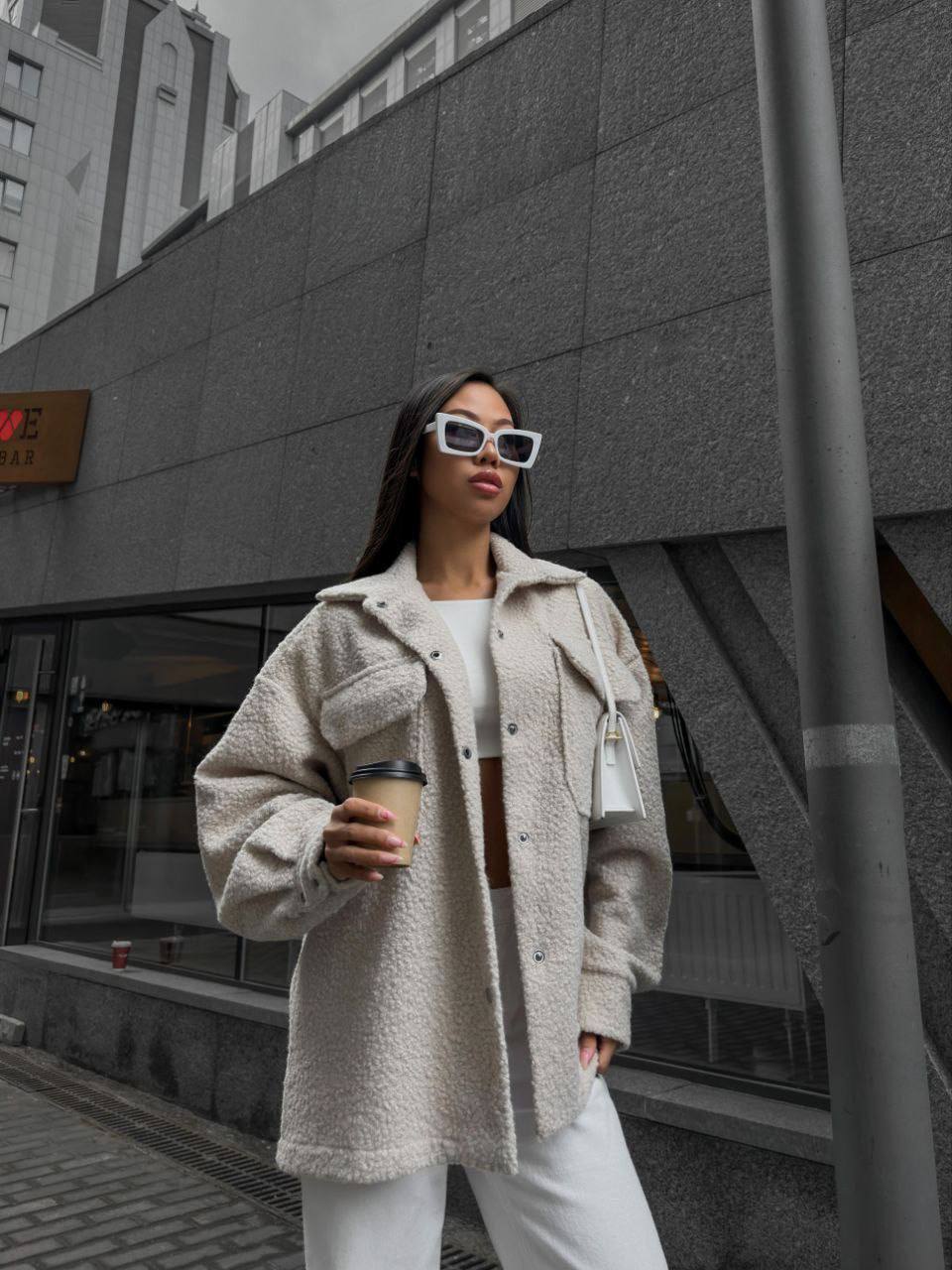 Woman in a beige coat holding a coffee cup against an urban background