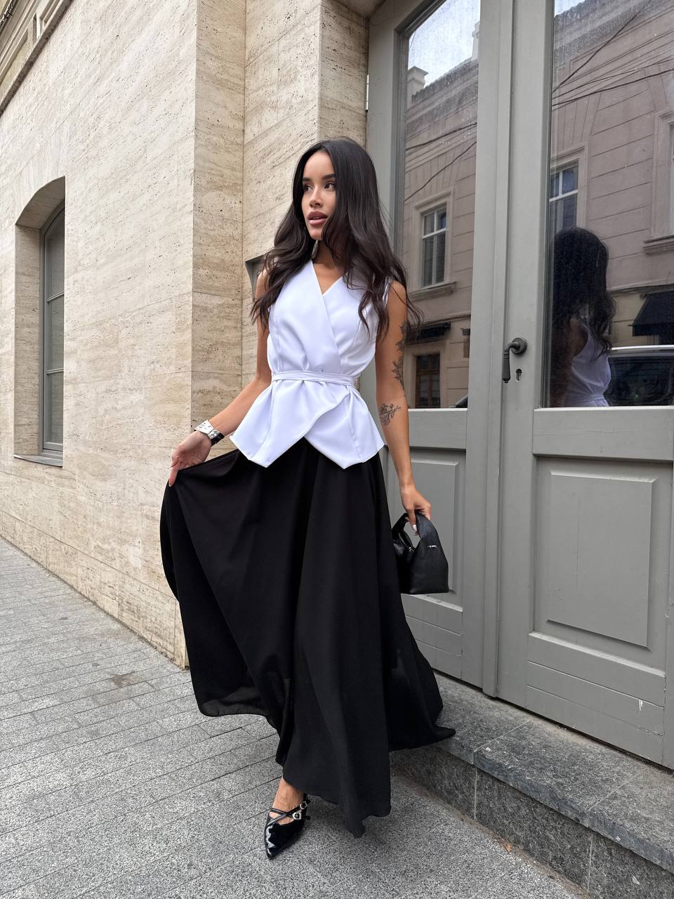 Woman in a white top and black skirt standing on a sidewalk.