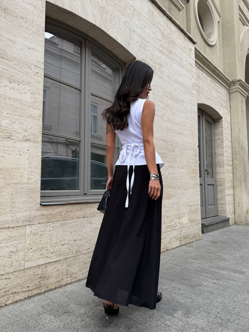 Woman in a white top and black skirt standing against a beige building.