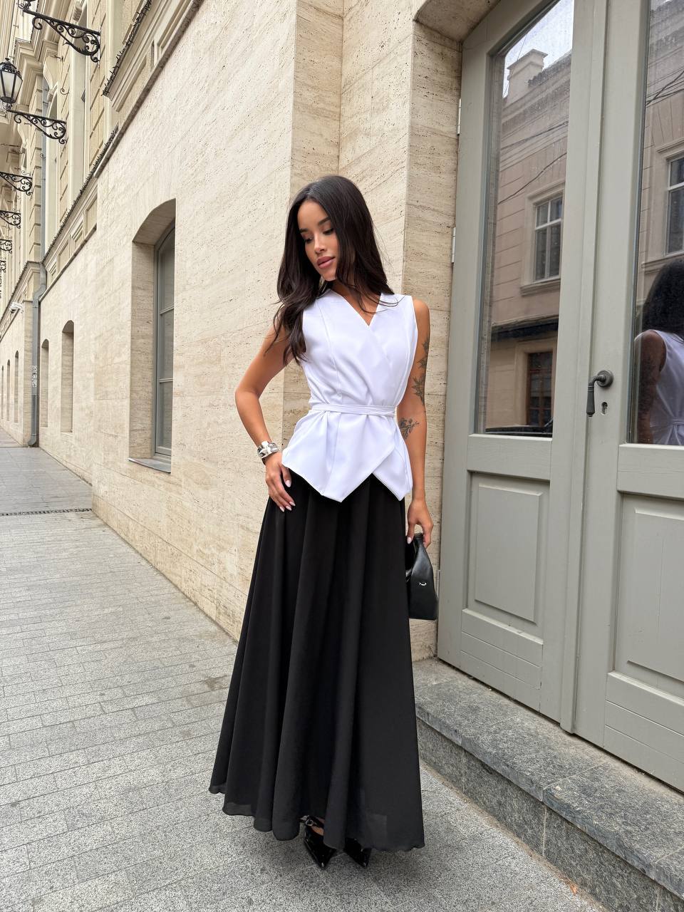 Woman wearing a white blouse and black skirt standing on a street.