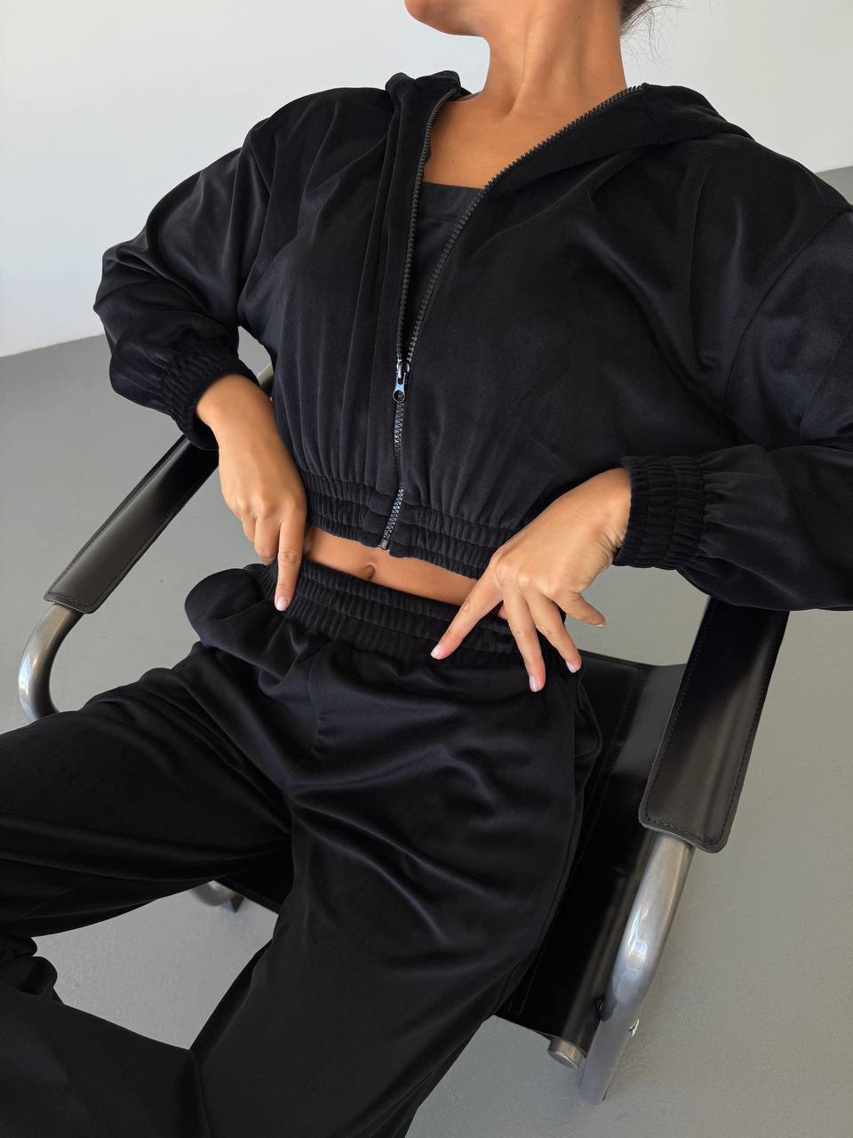 Person wearing a black cropped hoodie and pants sitting on a chair.