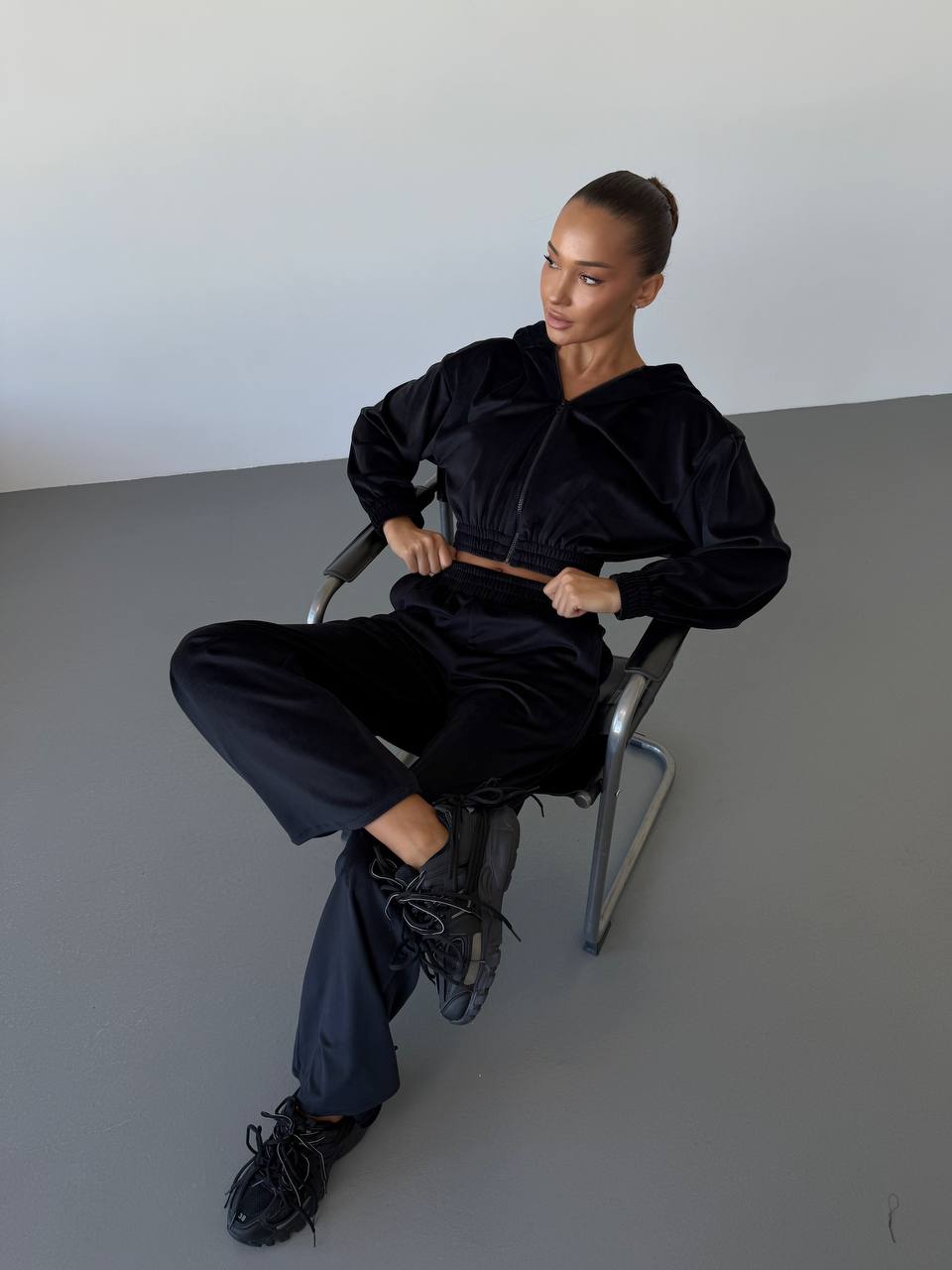 Person wearing a black outfit sitting on a chair against a plain background