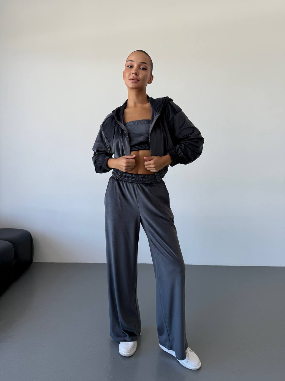 Person wearing a black tracksuit standing against a plain white wall.