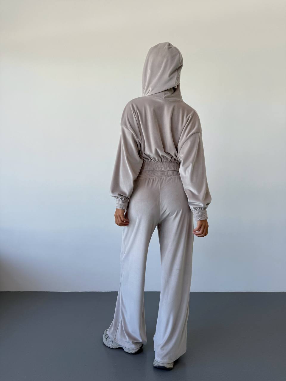 Person wearing a beige tracksuit standing against a plain white wall.