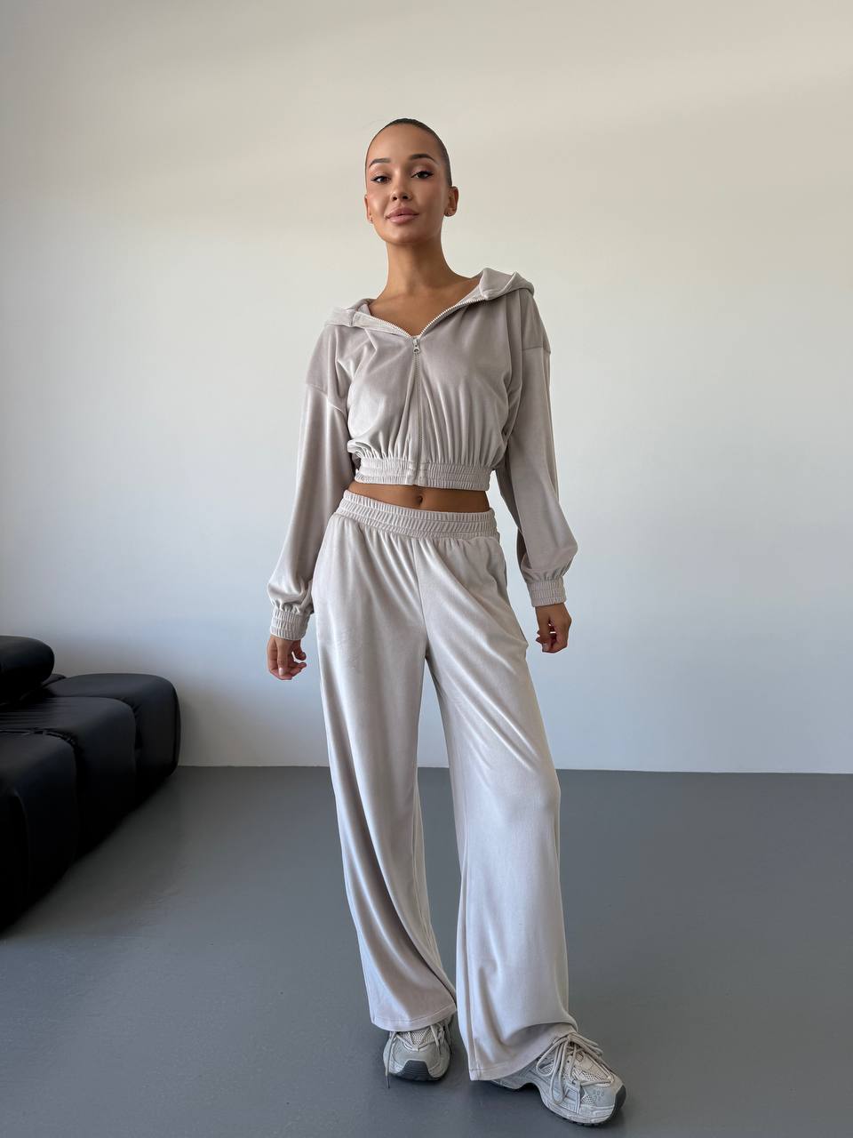Person wearing a light gray outfit with a cropped top and wide-leg pants in a minimal room.