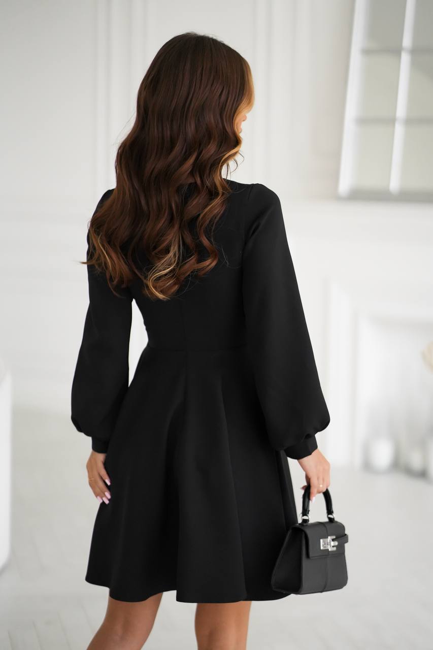 Woman wearing a black dress holding a black handbag in a minimalistic setting