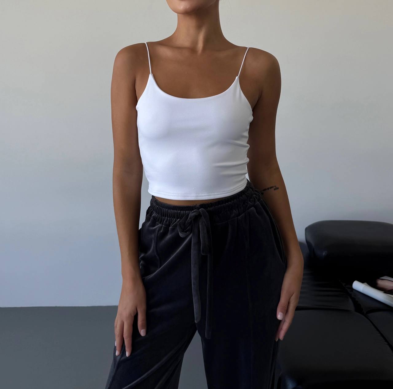 Person wearing a white tank top and black pants against a plain background