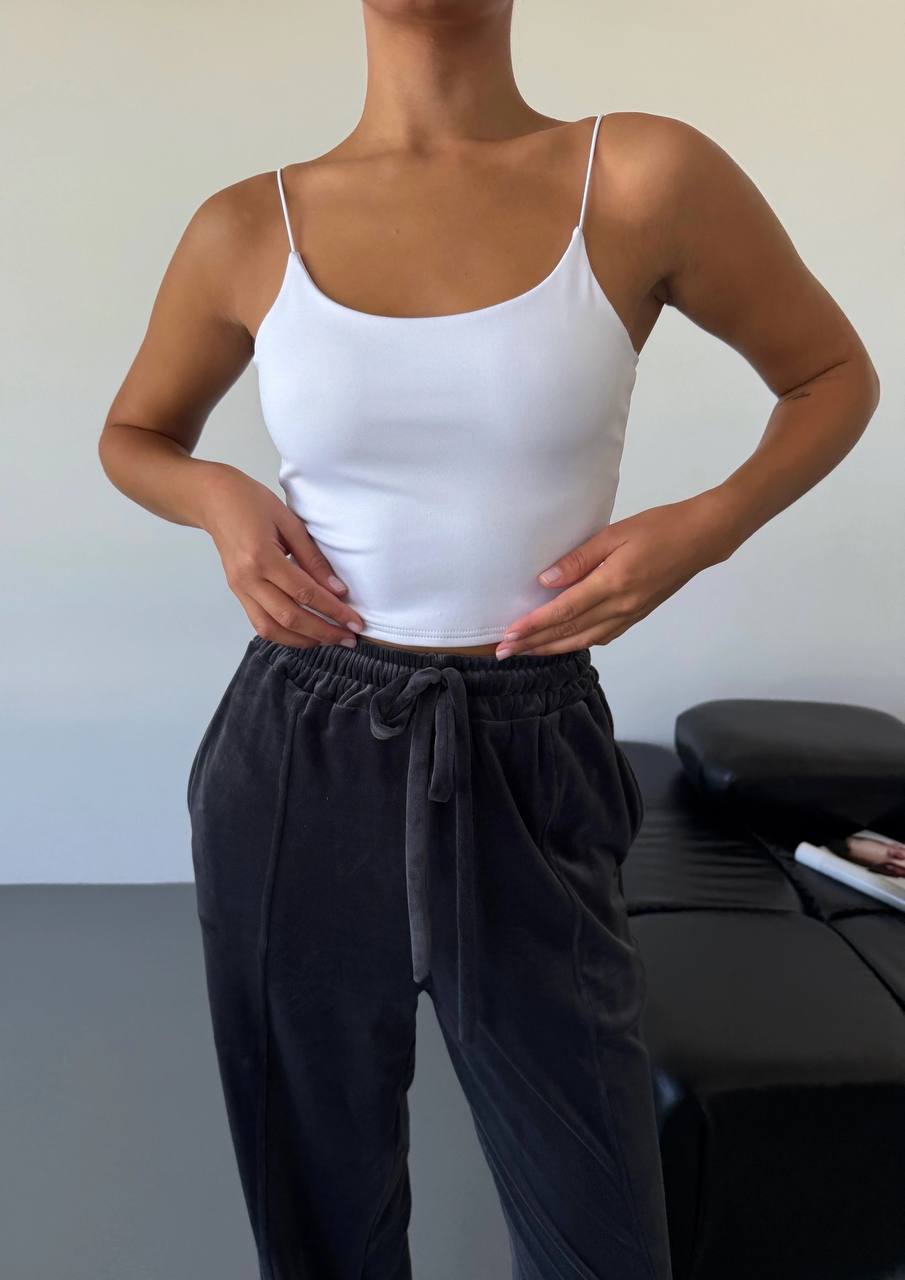 Person wearing a white tank top and black pants against a neutral background
