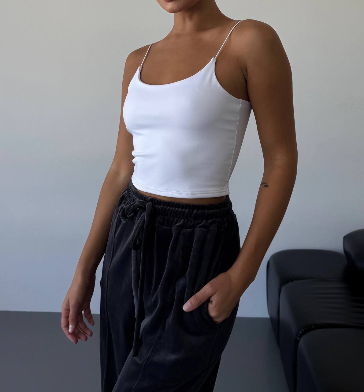Person wearing a white tank top and black pants against a neutral background