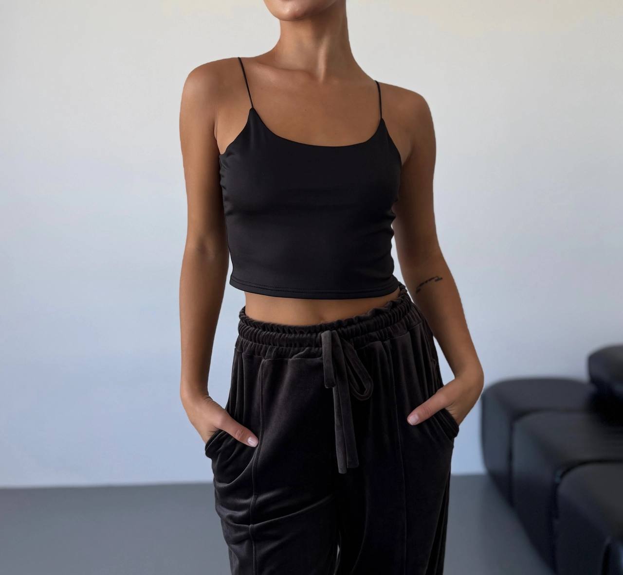 Person wearing a black tank top and black pants against a neutral background
