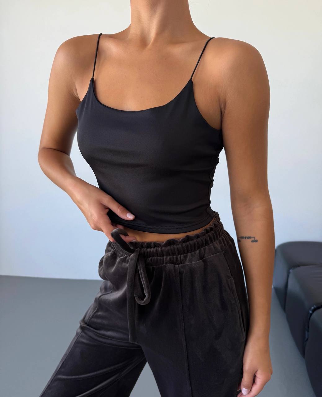 Person wearing a black tank top and black pants against a neutral background
