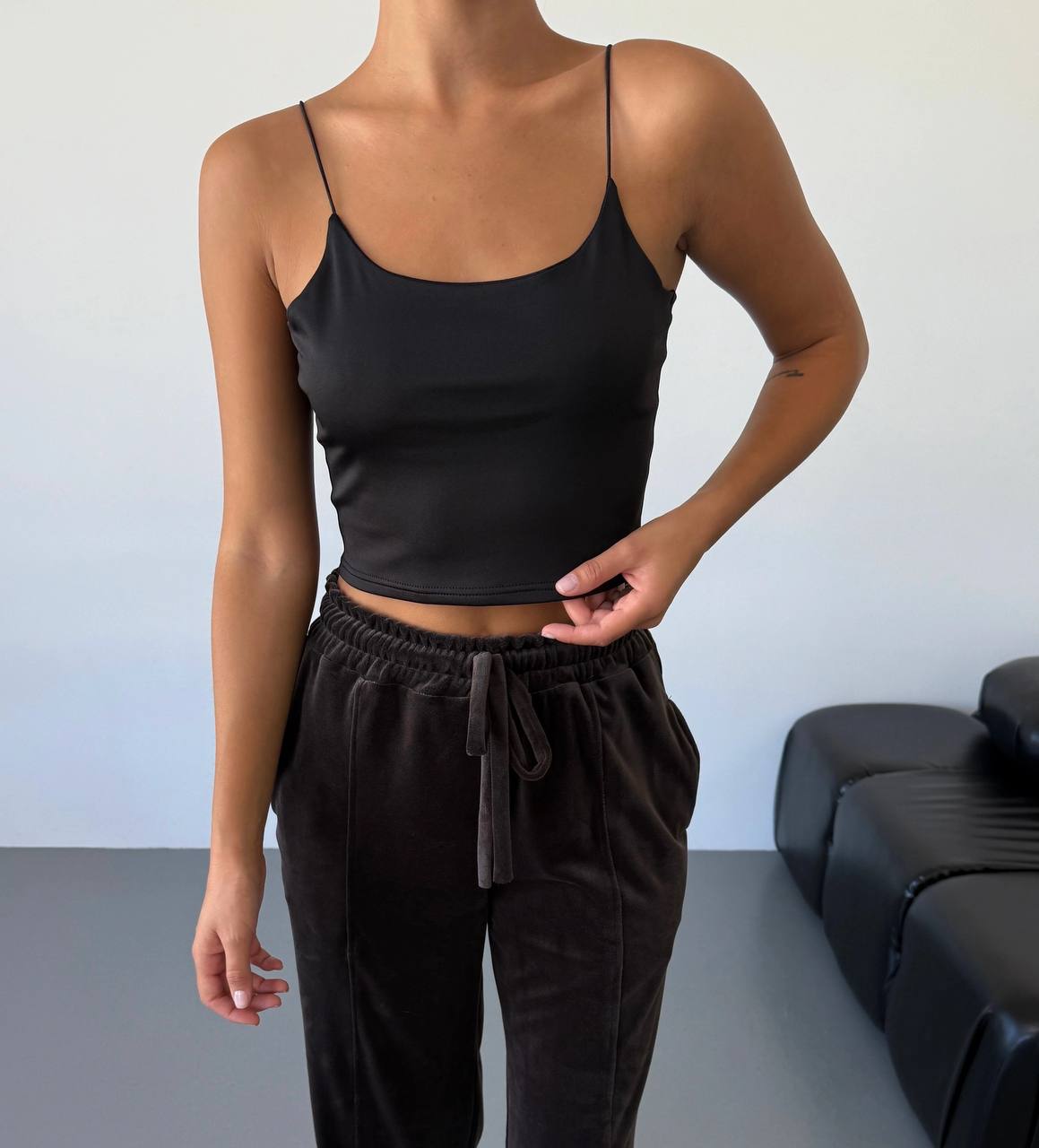 Person wearing a black tank top and brown pants in a minimal indoor setting