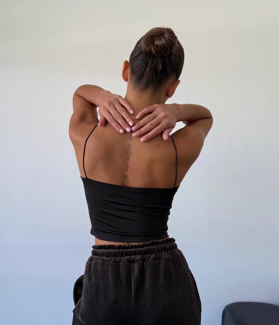 Person wearing a black tank top and pants, showing their back against a plain background