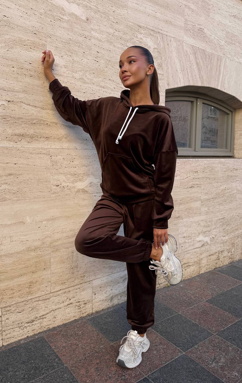 Person wearing a brown tracksuit leaning against a stone wall.