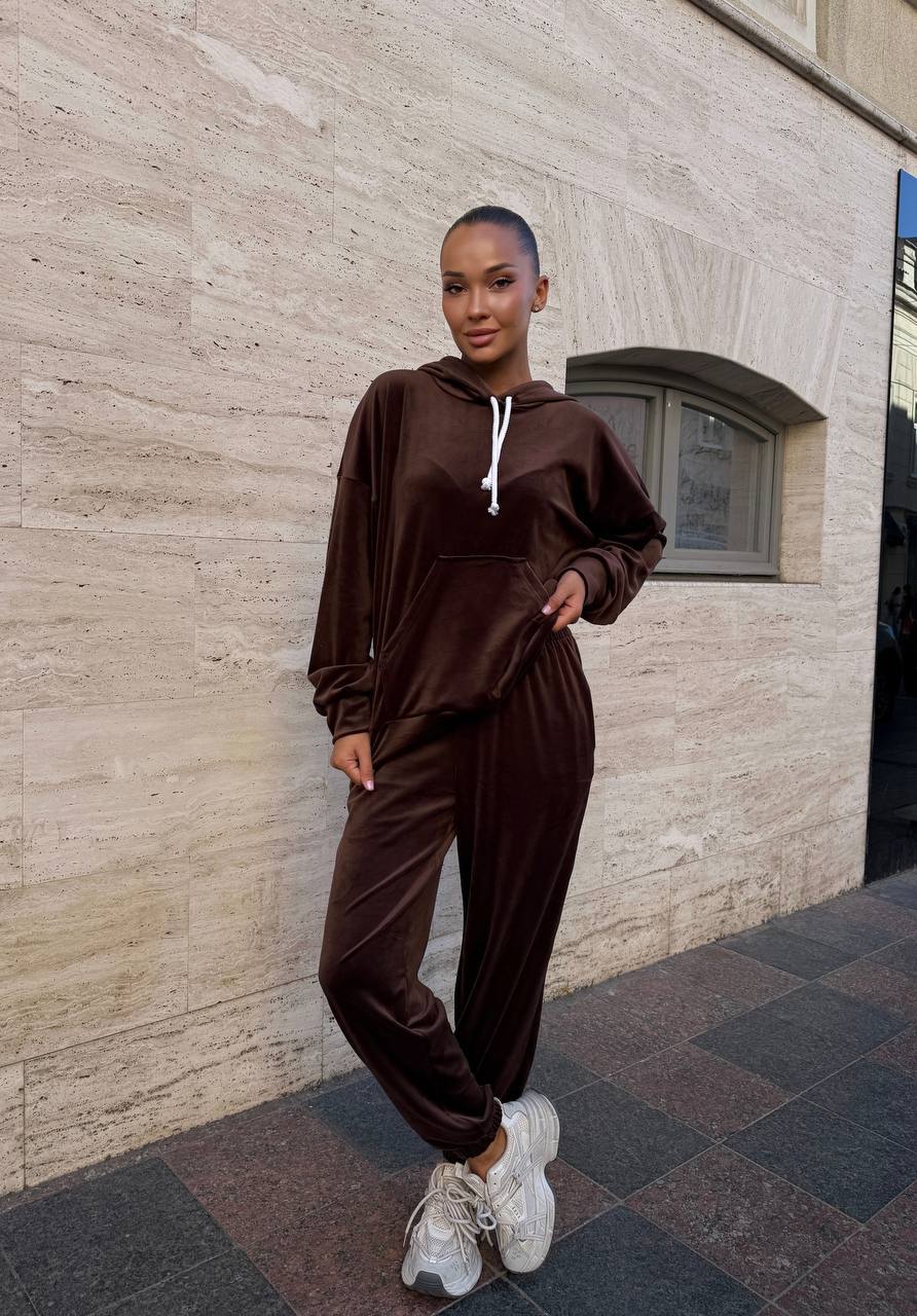 Person wearing a brown tracksuit standing against a stone wall.