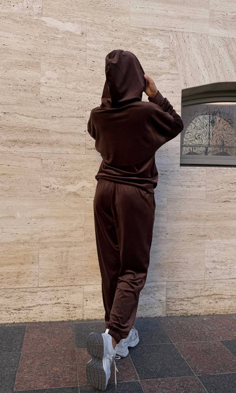 Person wearing a brown tracksuit standing against a beige wall.