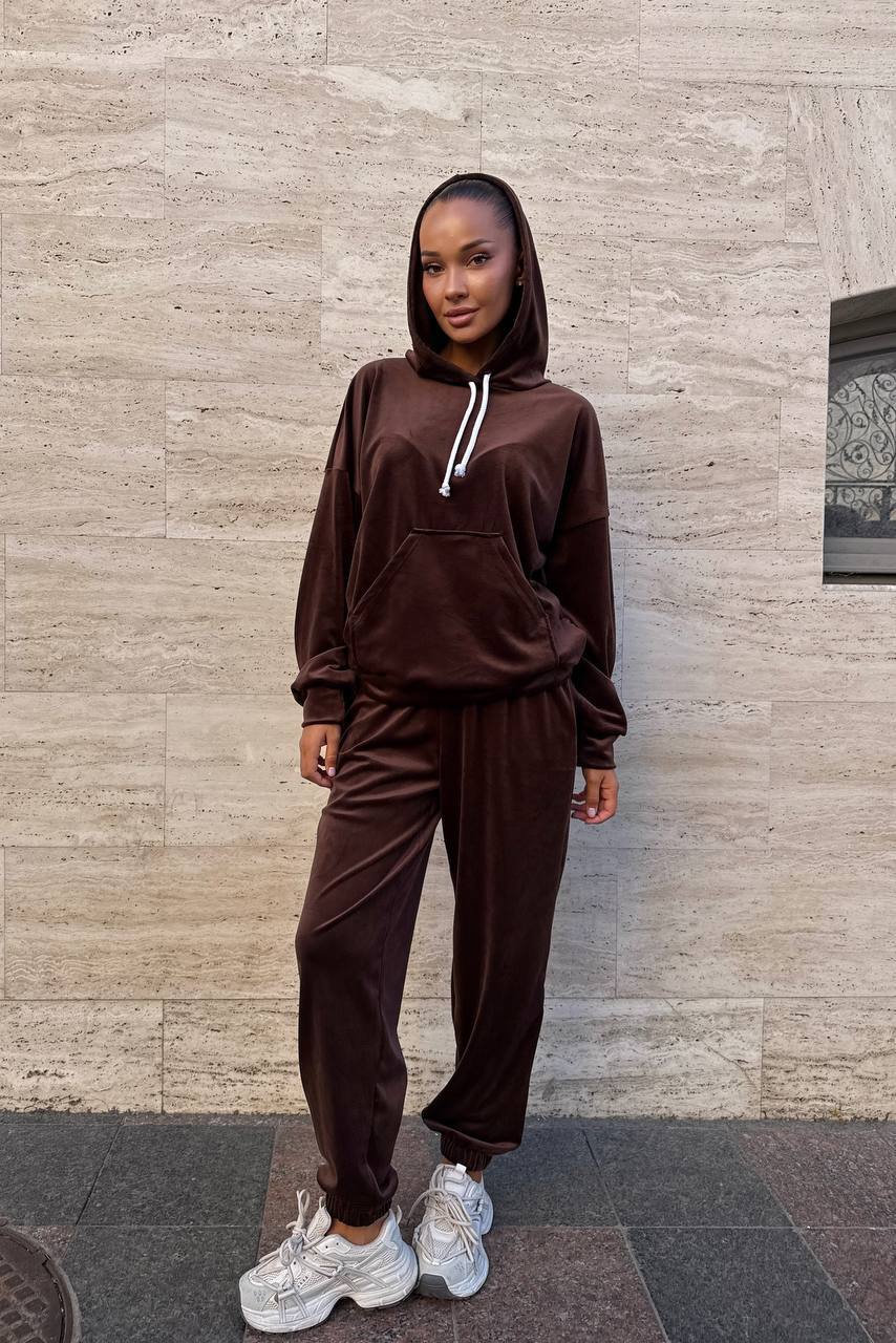 Person wearing a brown tracksuit standing against a stone wall.