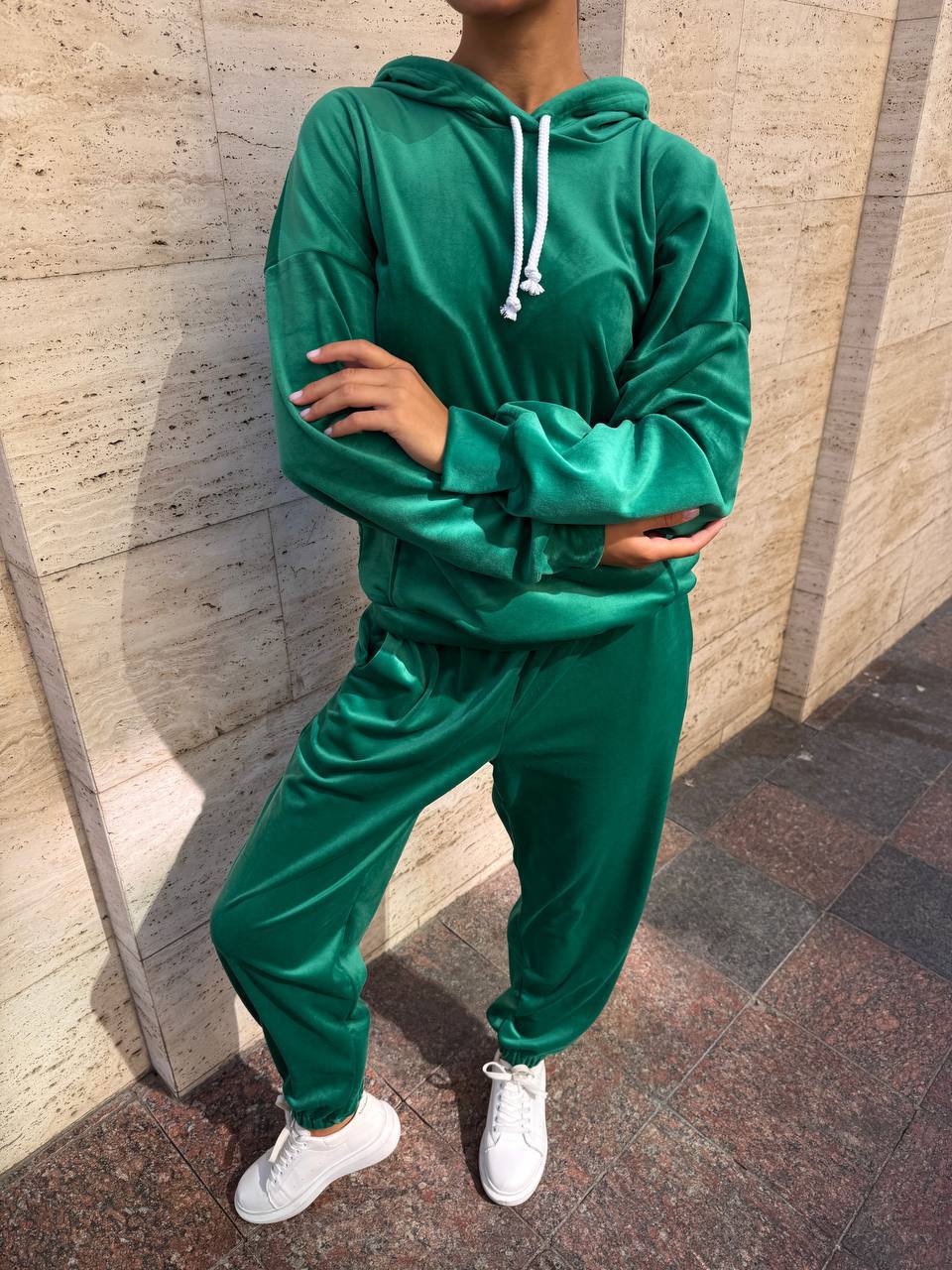 Person wearing a green tracksuit standing against a textured wall.