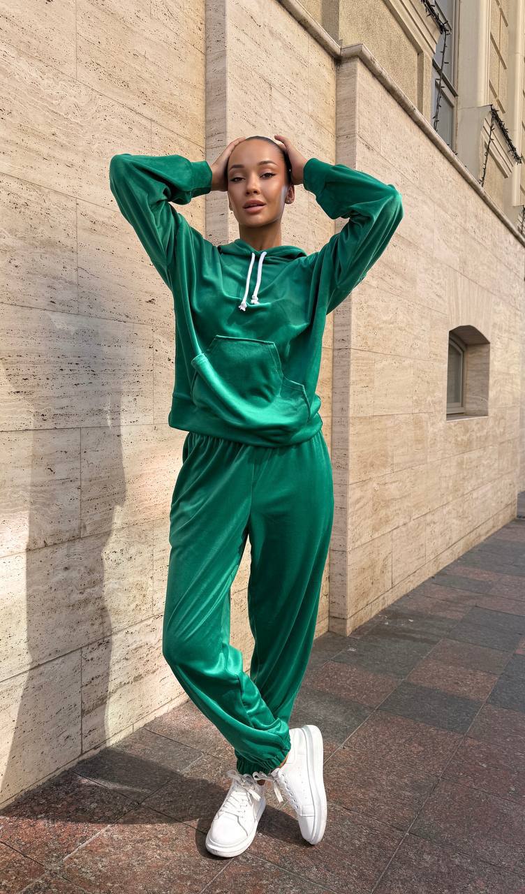 Person wearing a green tracksuit standing against a beige wall.