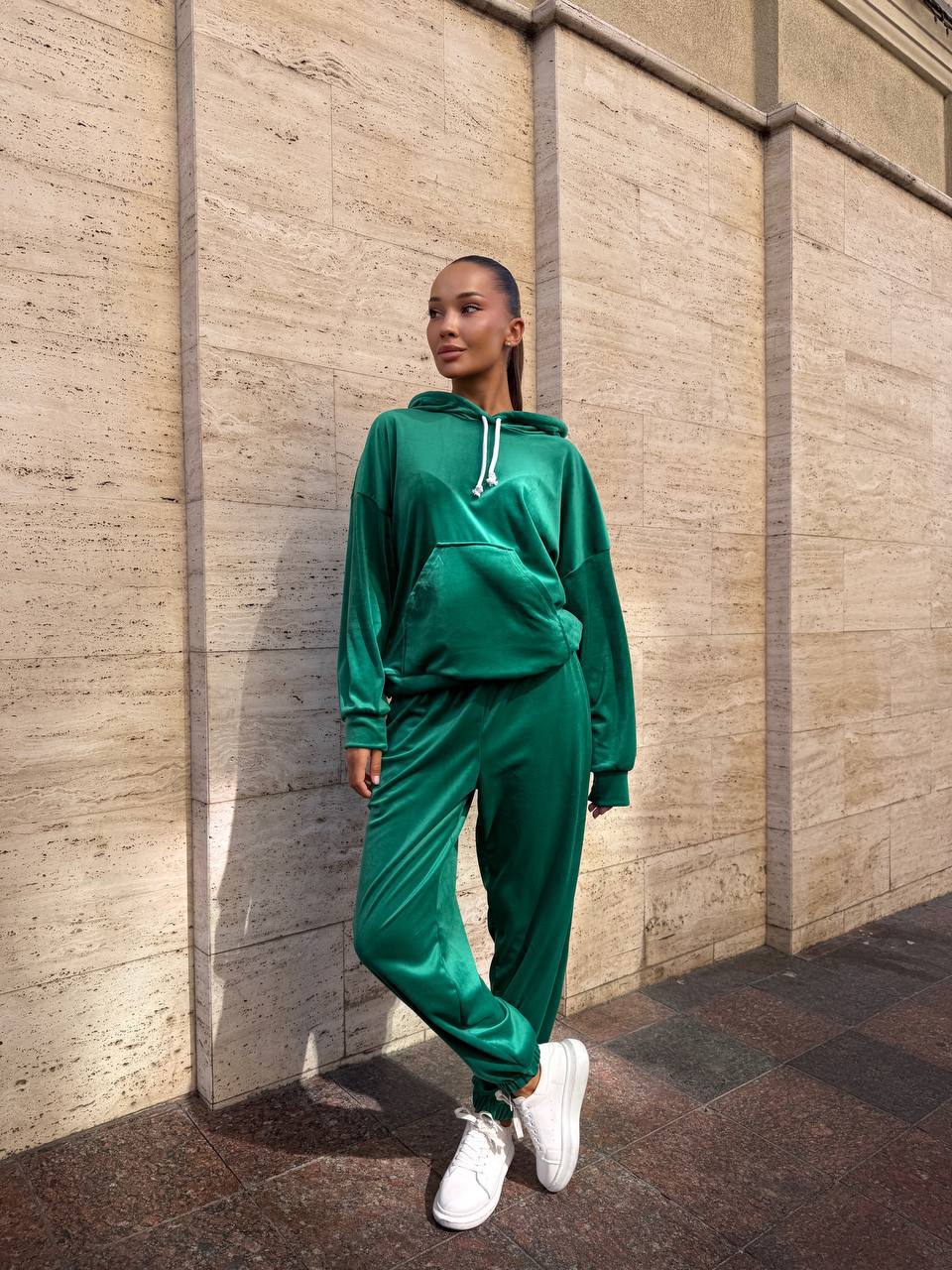 Person wearing a green tracksuit standing against a beige wall.