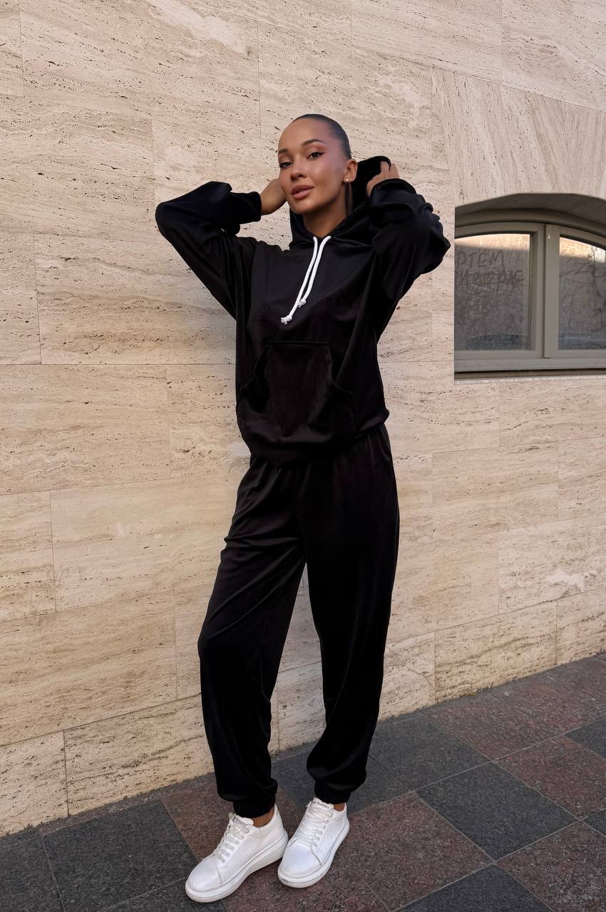 Person wearing a black tracksuit with white accents against a beige wall.