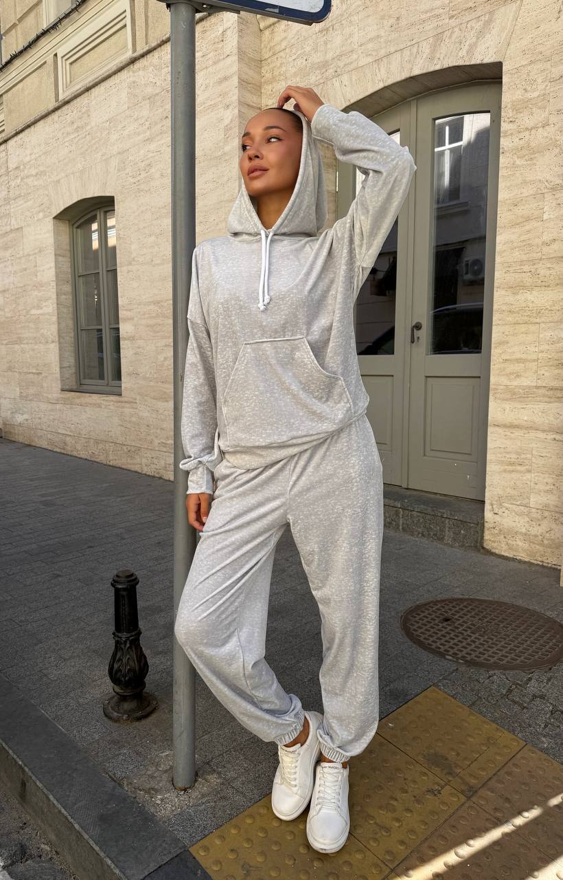 Person wearing a gray tracksuit standing on a sidewalk with a building in the background