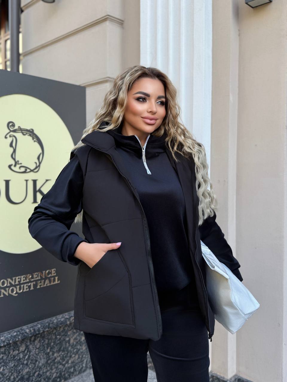 Woman wearing a black coat standing in front of a building with a sign.