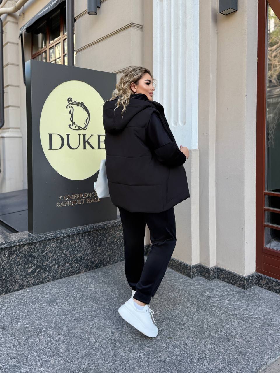 Person in black outfit standing outside a building with 'Duke' sign.