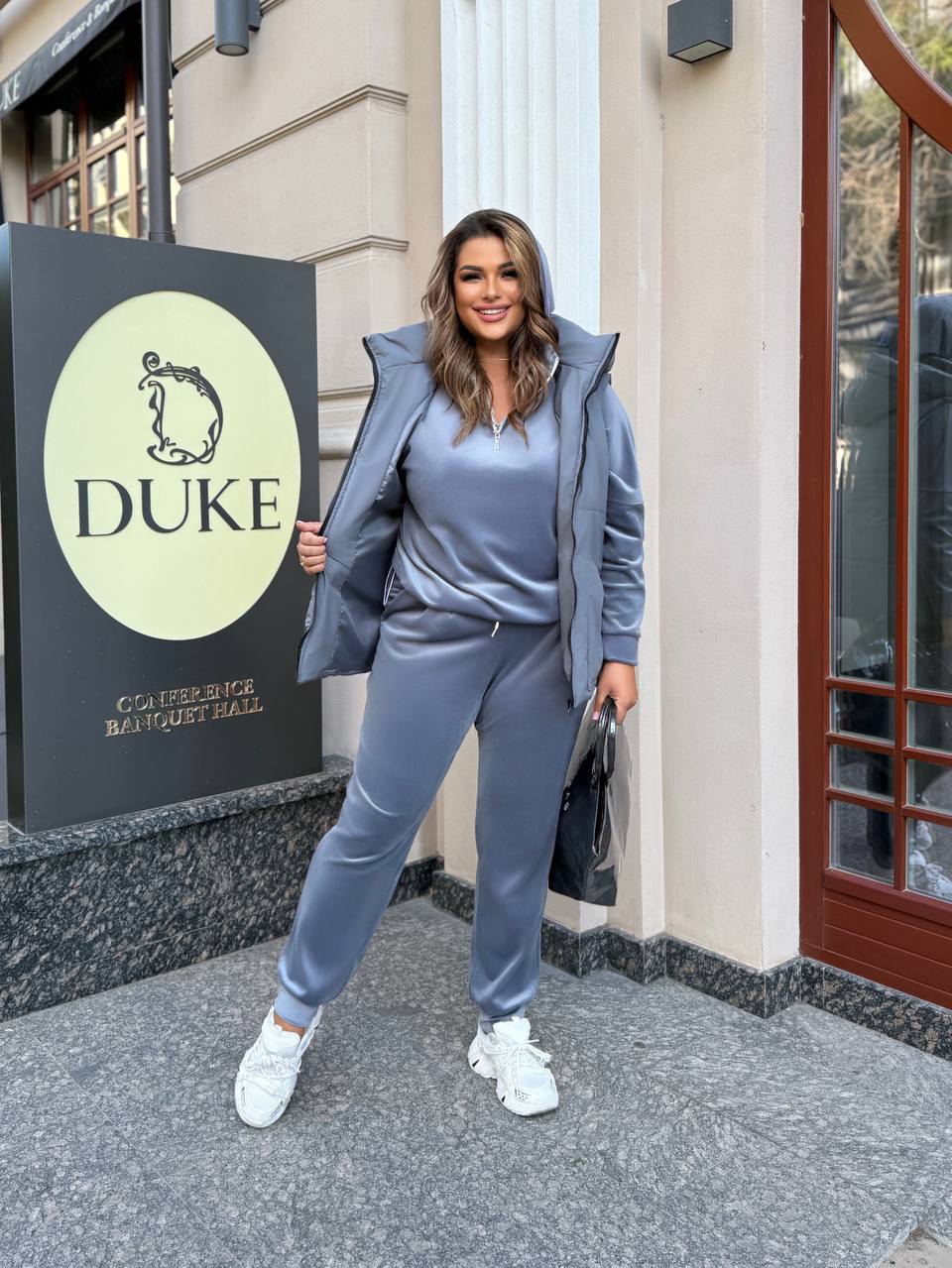 Woman in a gray tracksuit standing in front of a building with a 'Duke' sign.