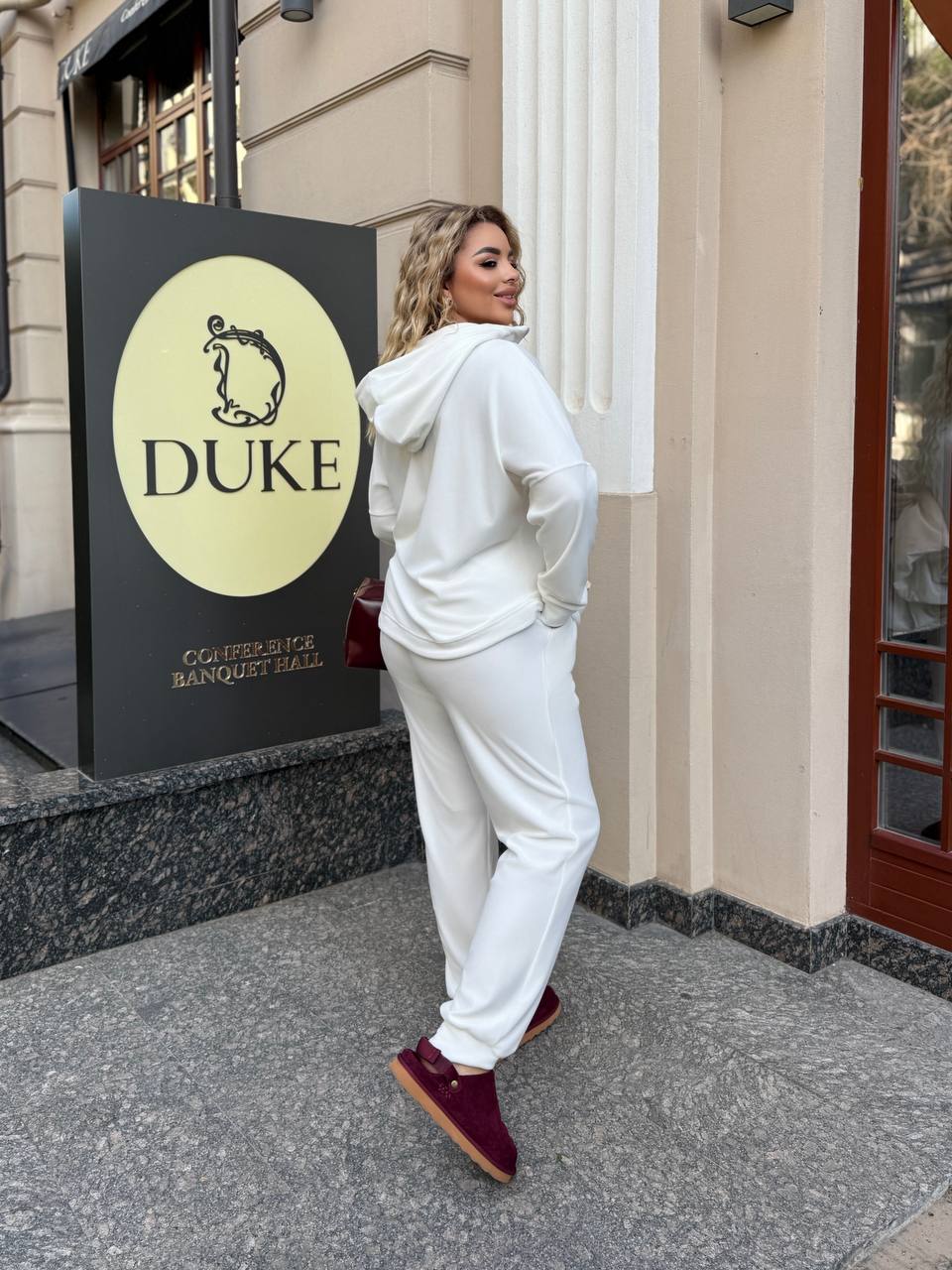 Person in a white outfit standing in front of a building with a 'DUKE' sign.