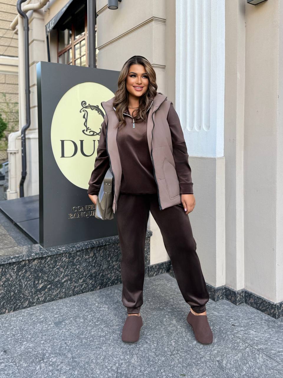 Woman in brown outfit standing outside a building with a sign in the background