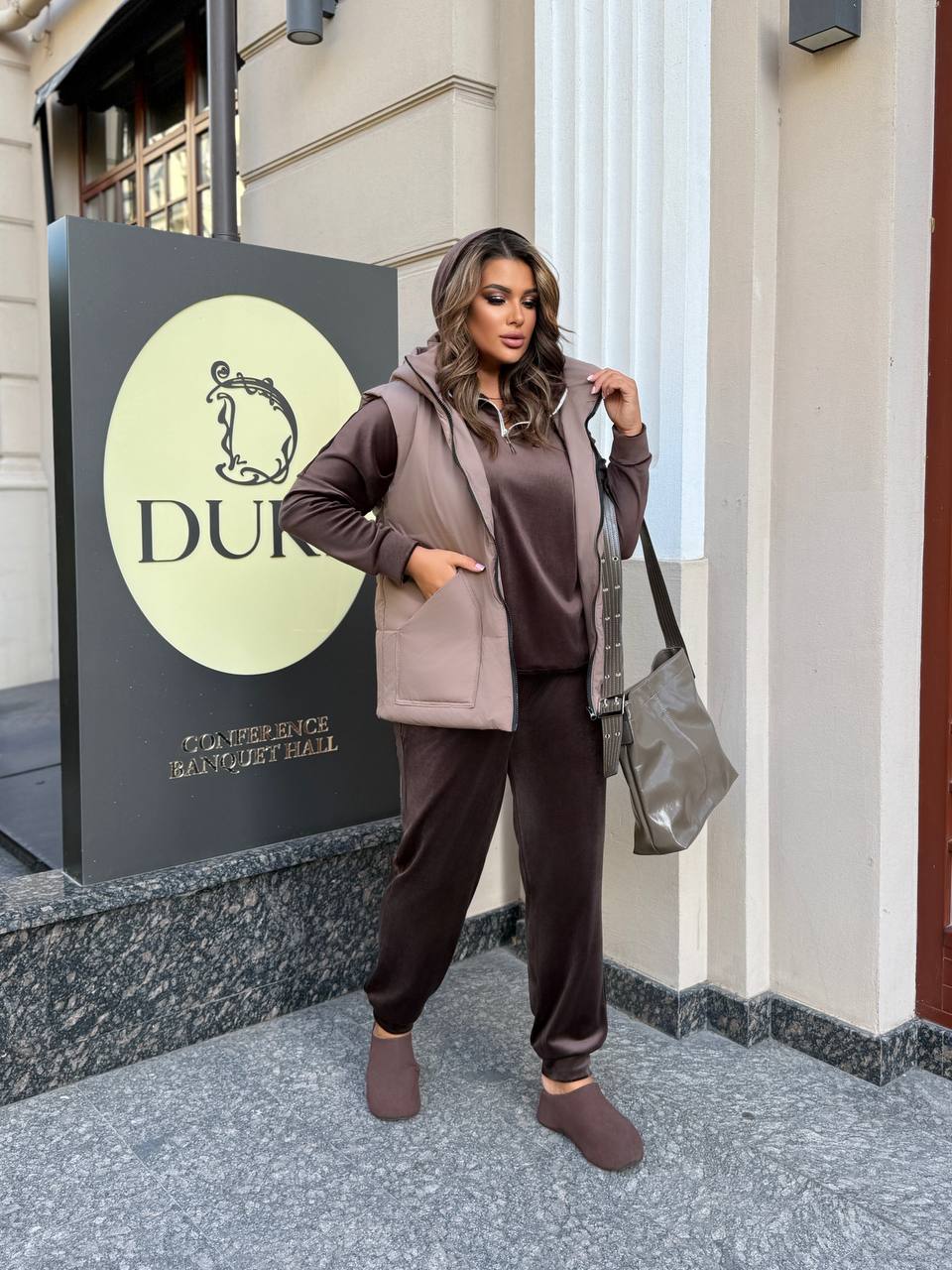 Woman in brown outfit standing outside a building with a sign that reads 'Dufy'.