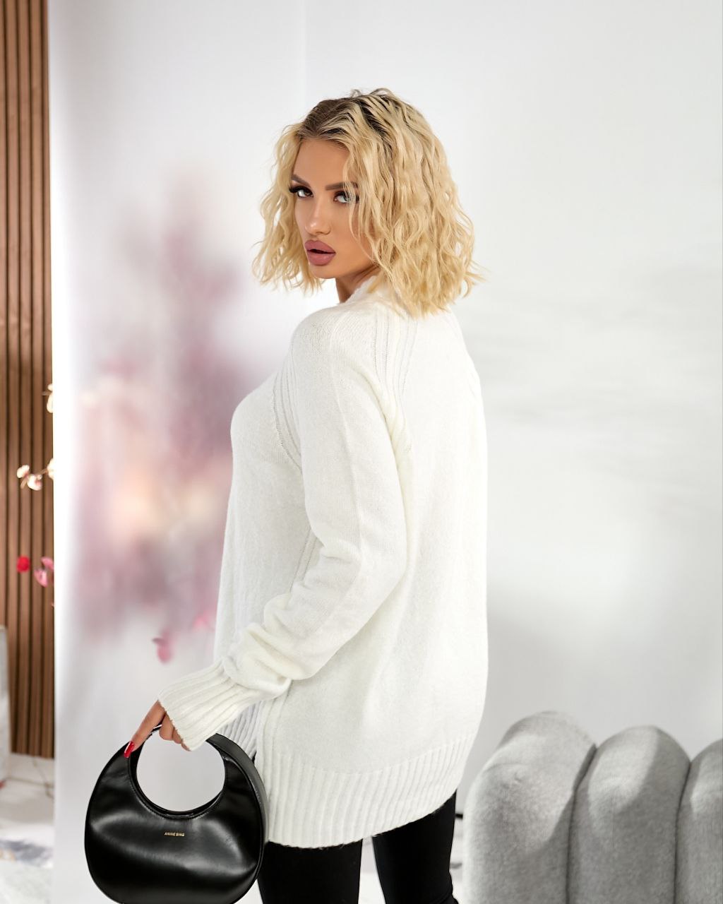 Woman wearing a white sweater holding a black handbag indoors.