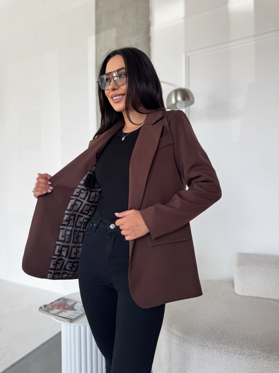 Woman wearing a brown blazer over a black outfit in a modern room.