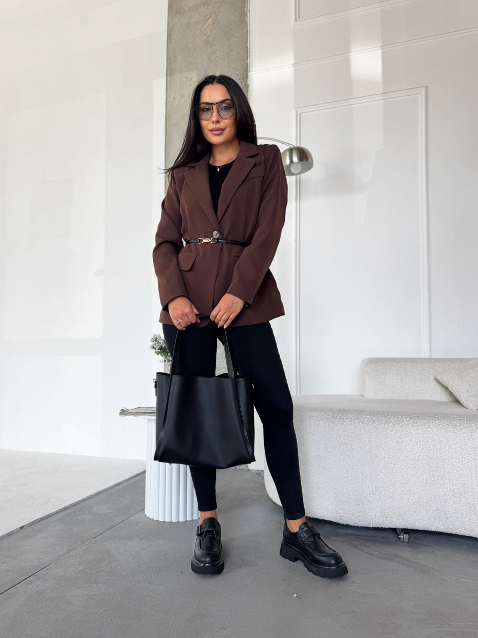 Woman in a brown coat with a black handbag in an indoor setting