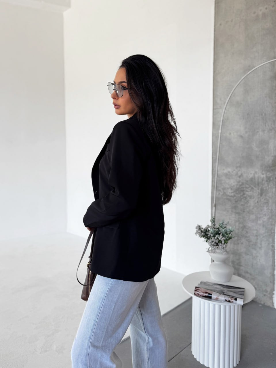 Woman in black top and light blue pants standing in a modern interior setting.
