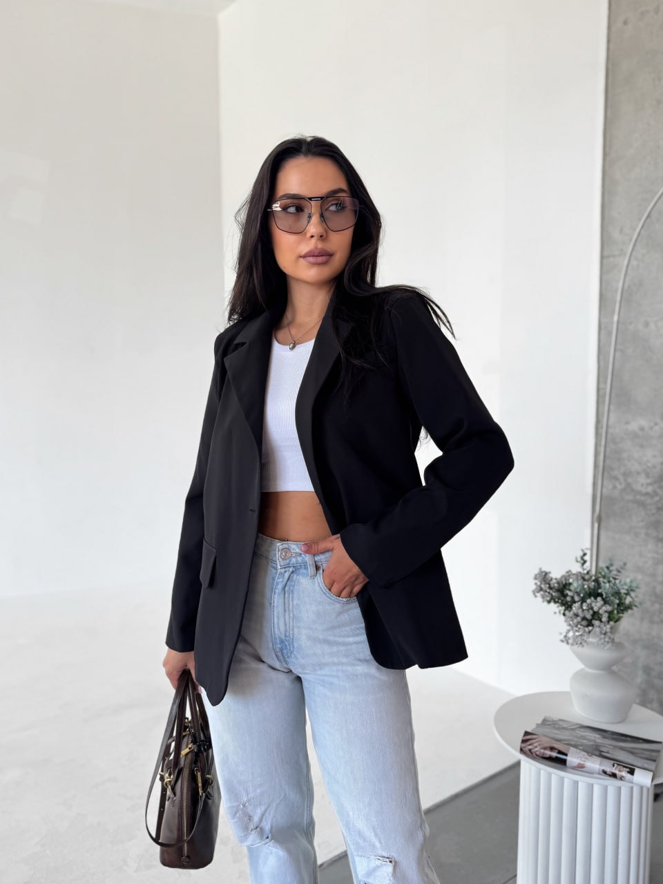 Woman wearing a black blazer, white top, and light blue jeans indoors.