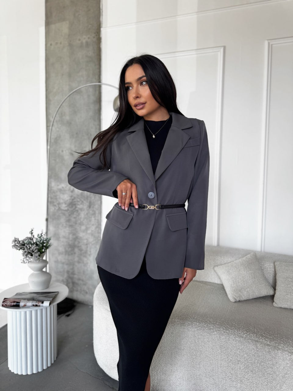 Woman in a gray blazer and black pants standing in a modern living room.
