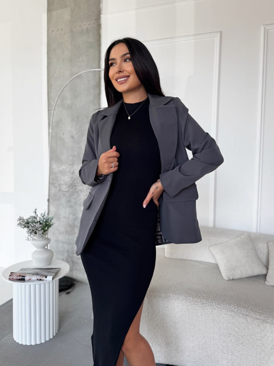 Woman wearing a gray blazer over a black dress in a modern living room.