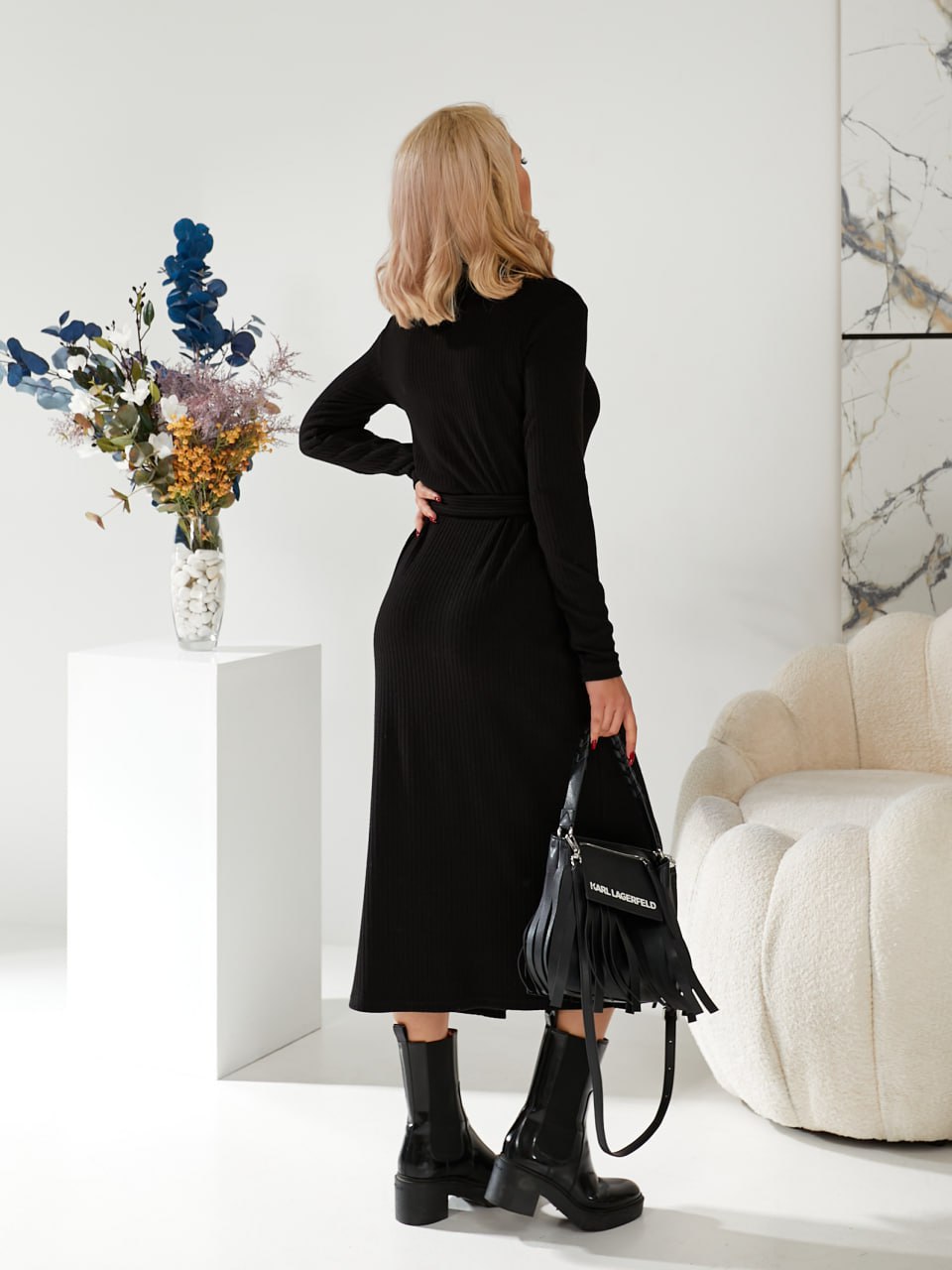 Woman in a black dress holding a black handbag in a minimalistic room.