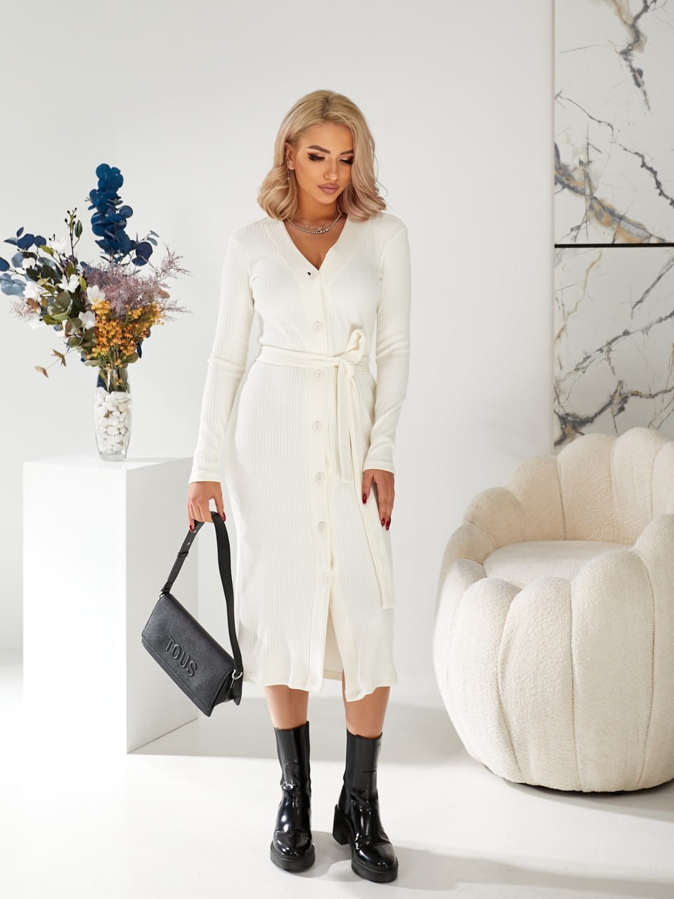 Woman in a white dress holding a black handbag in a modern interior setting