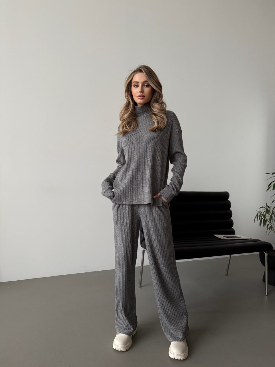Woman wearing a gray knit outfit in a minimalistic room.