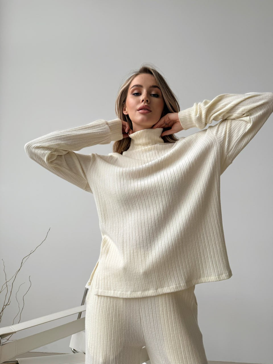Woman wearing a cream ribbed sweater and pants against a plain background