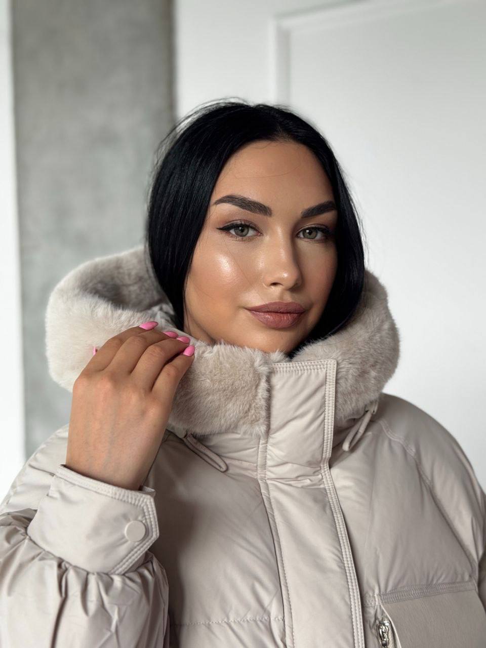 Woman wearing a beige winter coat with a fur-lined hood against a white background