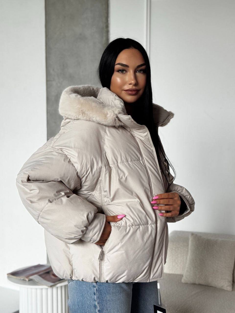 Woman wearing a beige puffer jacket with fur hood in an indoor setting