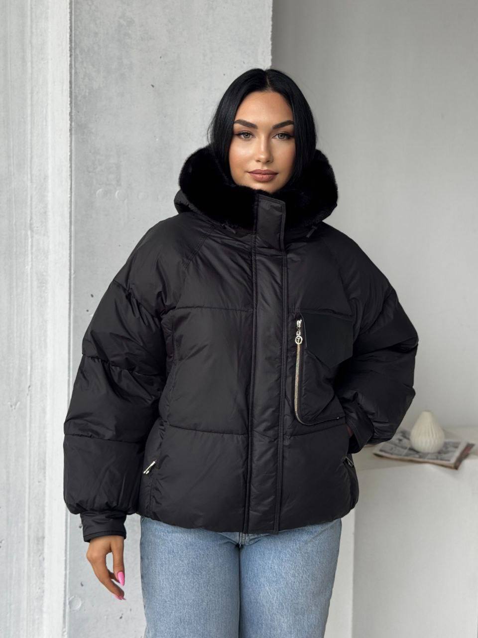 Person wearing a black puffer jacket with fur hood against a neutral background